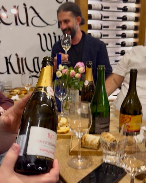 Photos inside In Vino wine bar in Yerevan, including a hand holding a bottle of Trinity Canyon Areni Noir, staff pouring wine behind shelves stocked with Armenian and international bottles, friends toasting with glasses of white wine, a long tasting table set with glassware beneath a sign reading 'The Renaissance of Armenian Wine Making,' and a wall of photos honoring winemakers