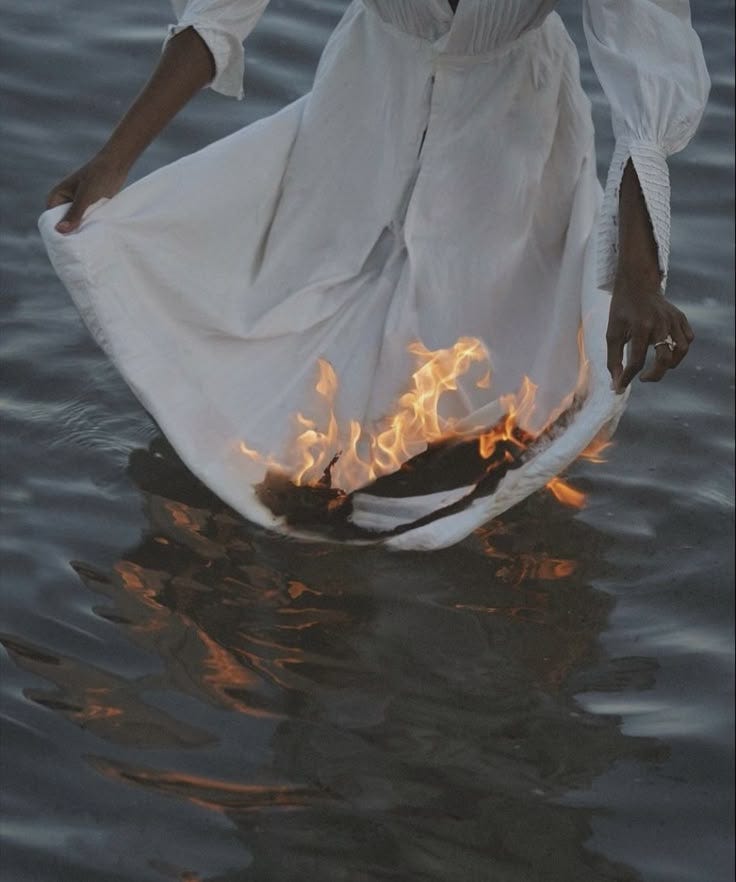 This may contain: a woman standing in the water with fire coming out of her pants and holding onto an object
