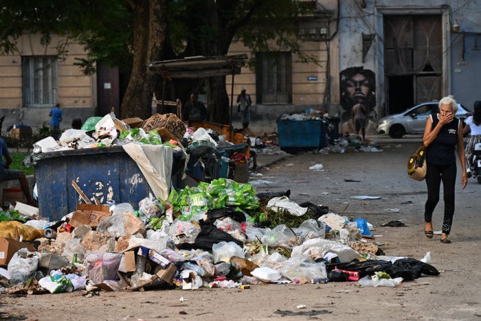A woman covers her nose while walking past piles of garbage on a street in Havana.