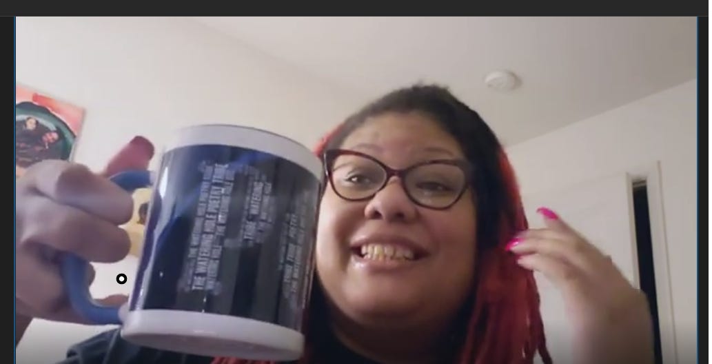 The image shows a me holding a mug with the text "THE WATERING HOLE POETRY"  I'm indoors, wearing glasses and smiling. 