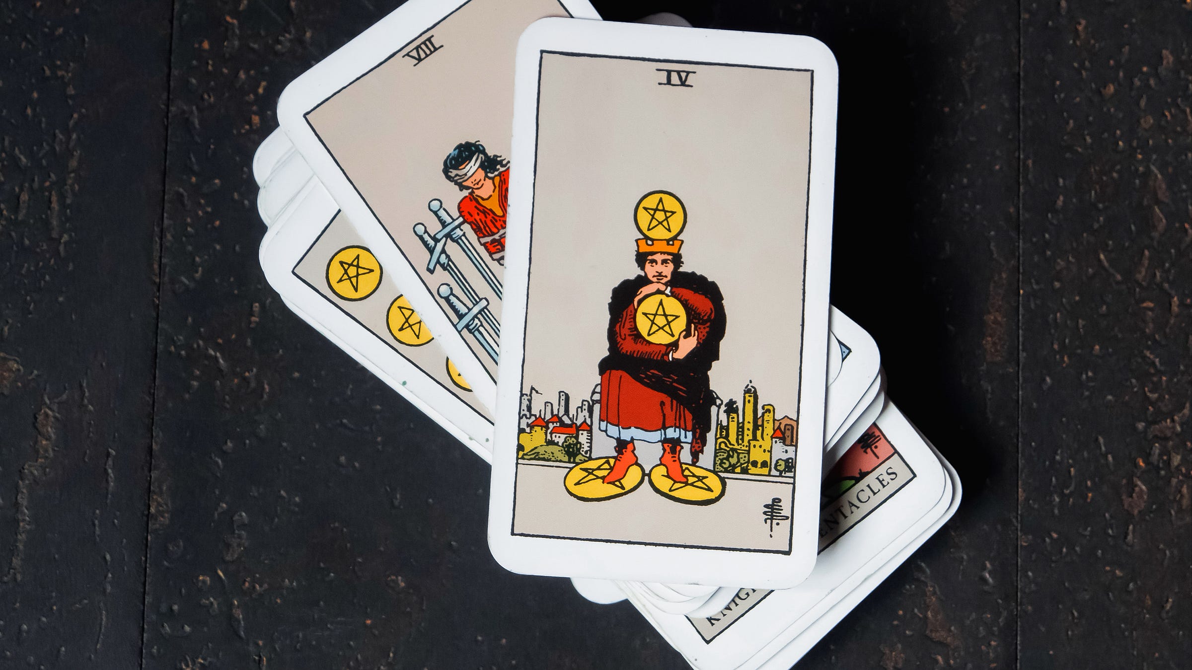 the four of pentacles card sitting on another stack of tarot cards from my very own rider waite tarot deck on a dark wood floor