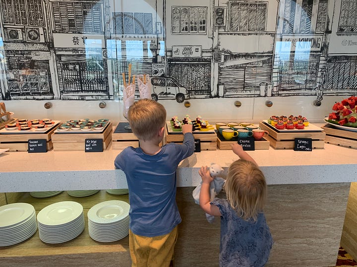 the exterior of an older hotel building versus the interior of a hotel with cakes and the backs of 2 children choosing something to eat.