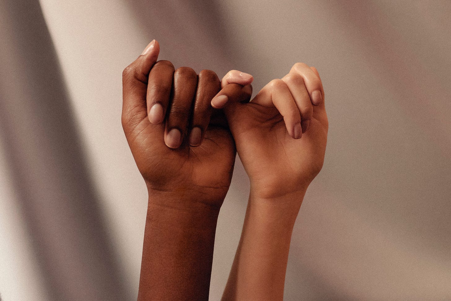 Two people hold their hands in the air, little fingers linked in a show of solidarity. One person is Black, the other is white. Two people hold their hands in the air, little fingers linked in a show of solidarity. One person is Black, the other is white.