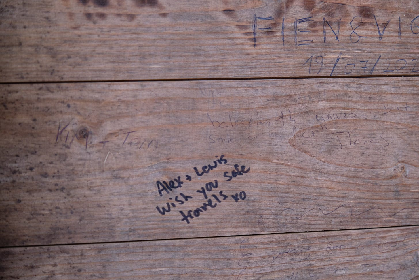 A wall inside a bothy covered with handwritten notes and messages left by visitors. At the centre, one note clearly wishes “safe travels” to future readers.
