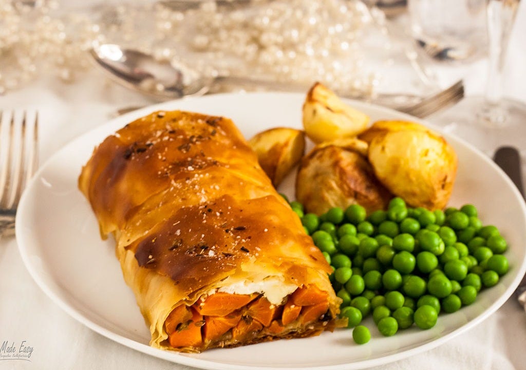Carrot and Feta Strudel on a white plate served with peas and potatoes