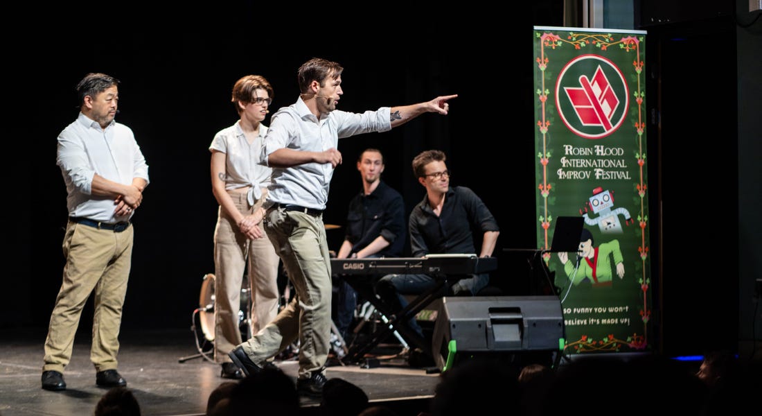 Five performers on stage - two sat down and three stood up - with a green banner to the right
