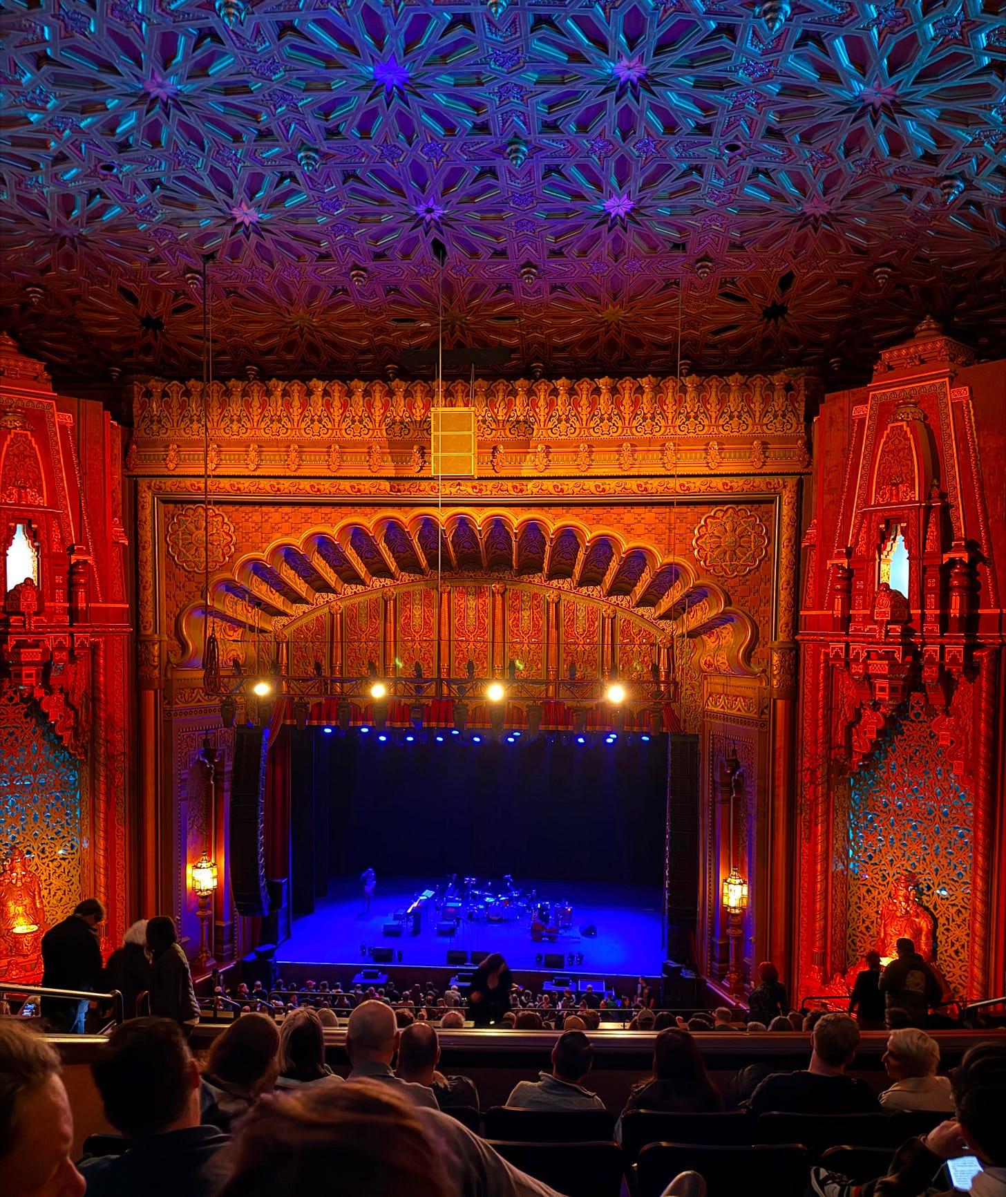 The Fox Theatre in Oakland looks haunted. The lights are very dimmed on the stage and there are people in the foreground. 