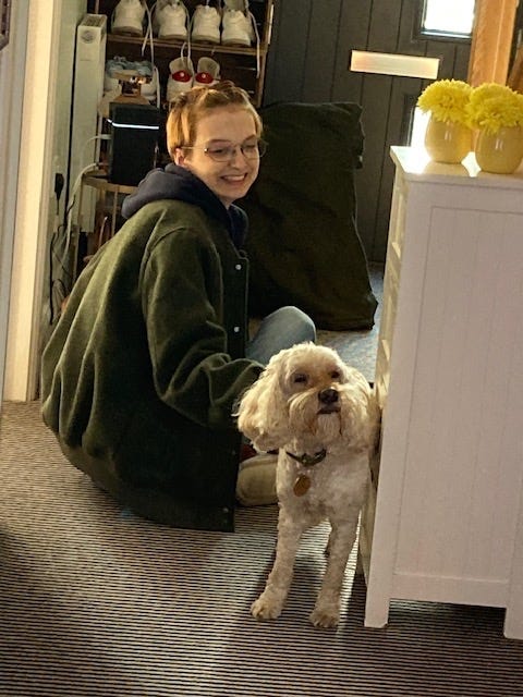 Beck sitting on the floor in a hallway, scratching Gibbs- an elderly cockapoo who is leaning into the belly scractches with his eyes closed
