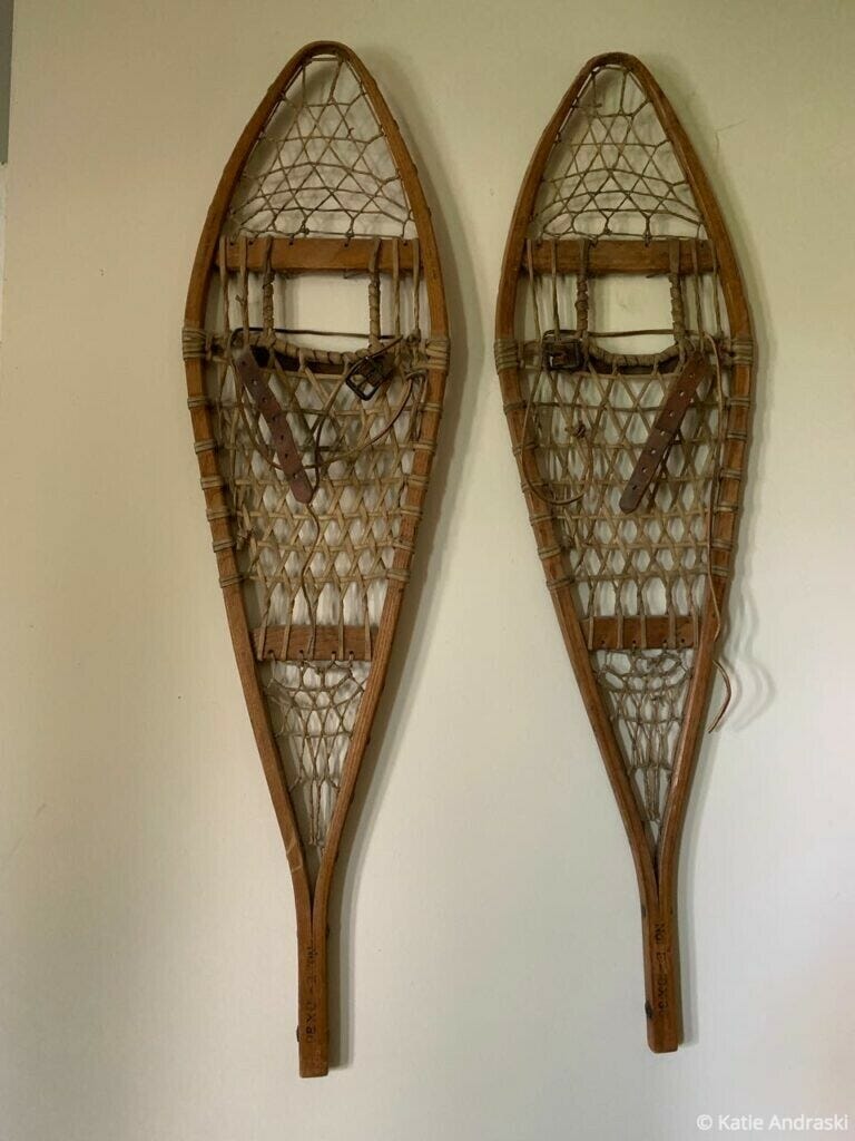 Pair of vintage wooden snowshoes hanging on a wall.
