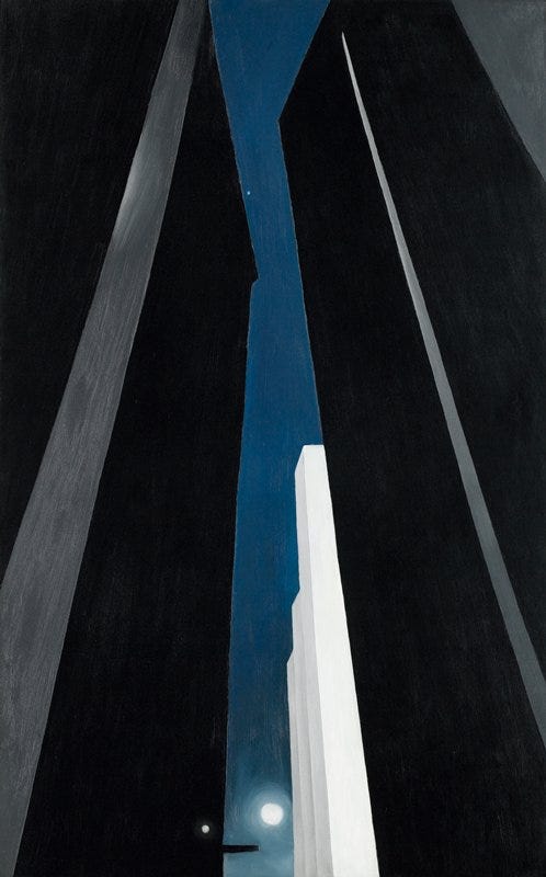Alt text: Tall, dark skyscrapers rise on either side of a narrow vertical strip of deep blue night sky, with a small white building catching moonlight near the bottom, creating a dramatic, upward-looking city canyon.