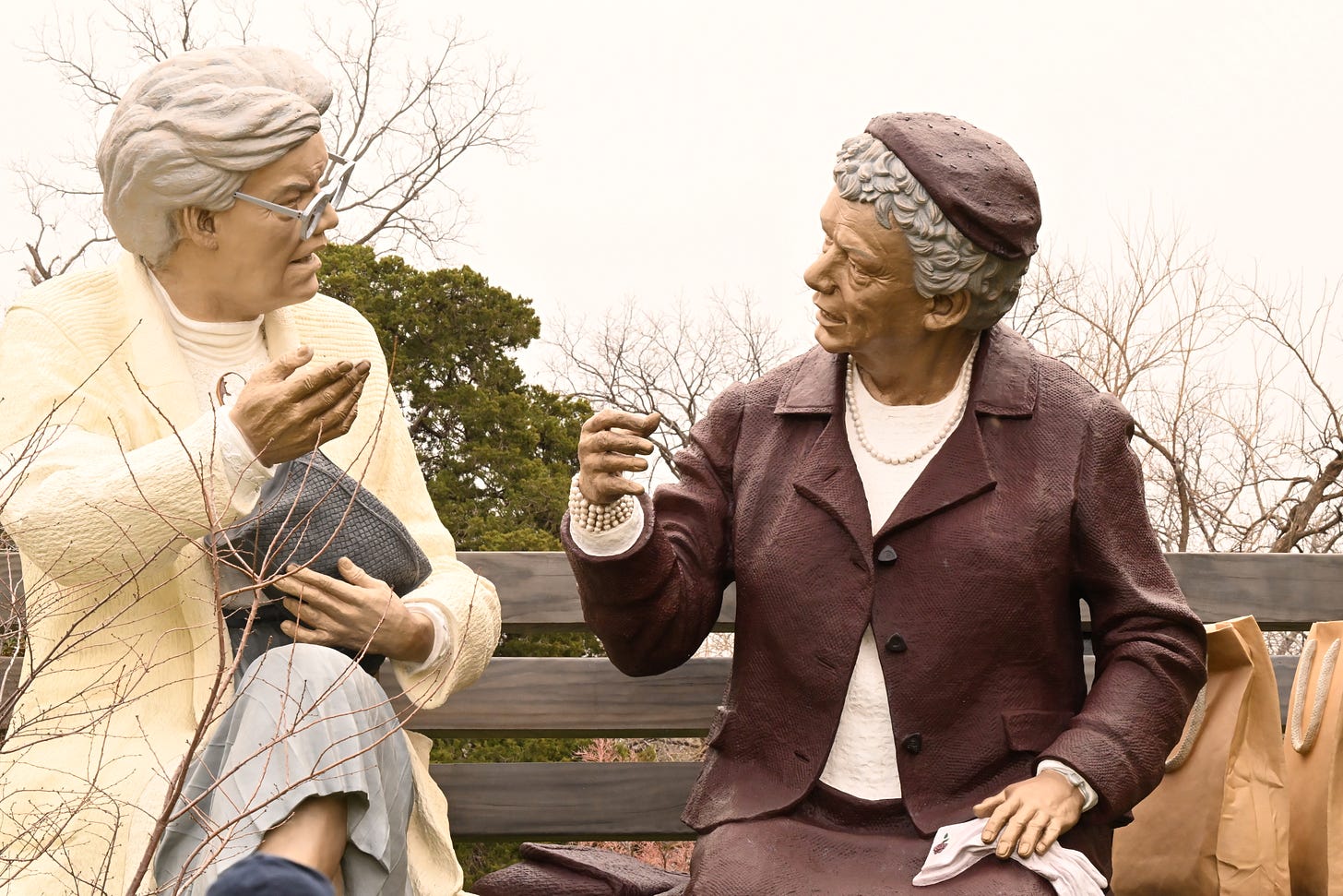 Larger than life sculpture of two old women chatting animatedly on a park bench