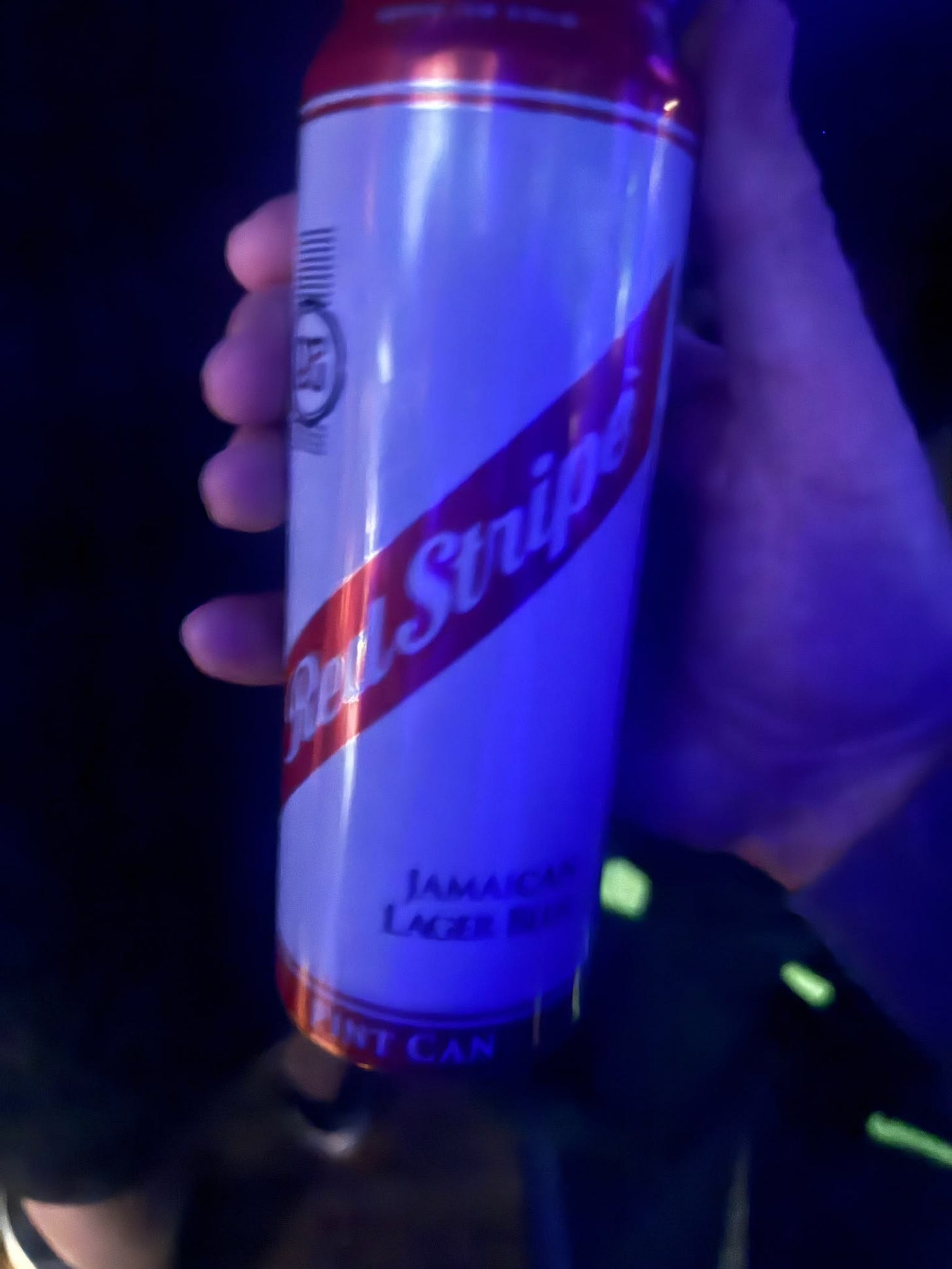 A pint can of Red Stripe held up in a dark gig venue