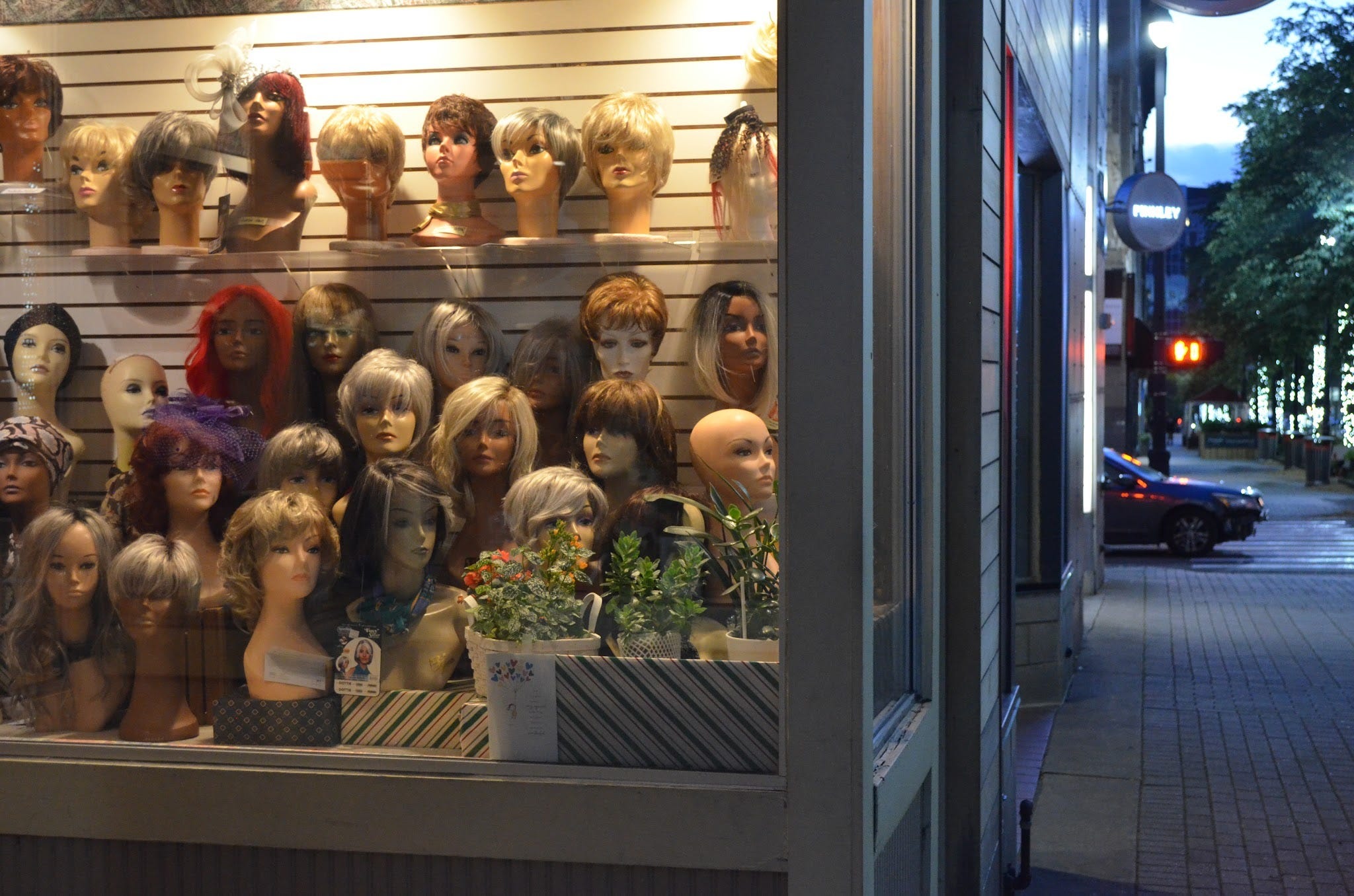 Wigs displayed in a shop window beside the sidewalk on Monroe Center, Grand Rapids.