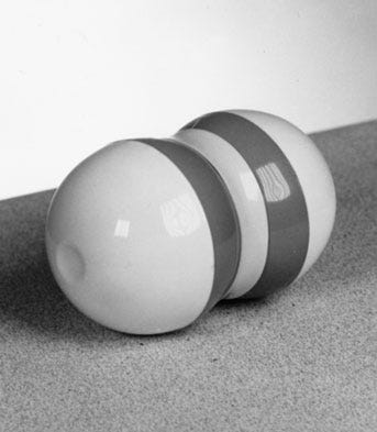 A black and white photo of a Zerret Applicator - a squat, dumbbell-like plastic object with two darker stripes on its white background.