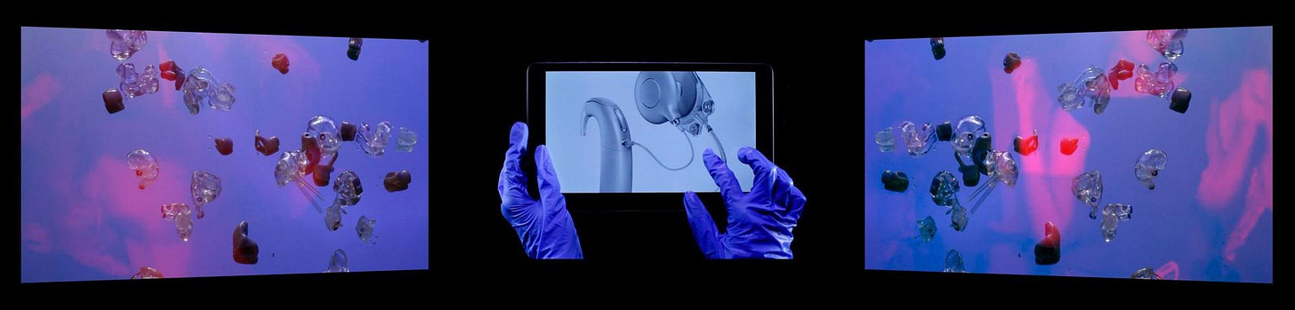 A three panel video installation features images of hearing aids floating in blues and pinks, with an image of hands in latex gloves interacting with a tablet displaying a closeup of a sleek hearing aid.
