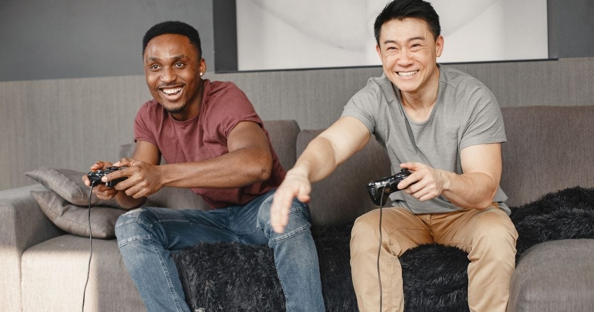 Two friends laughing and playing video games together on a comfortable sofa