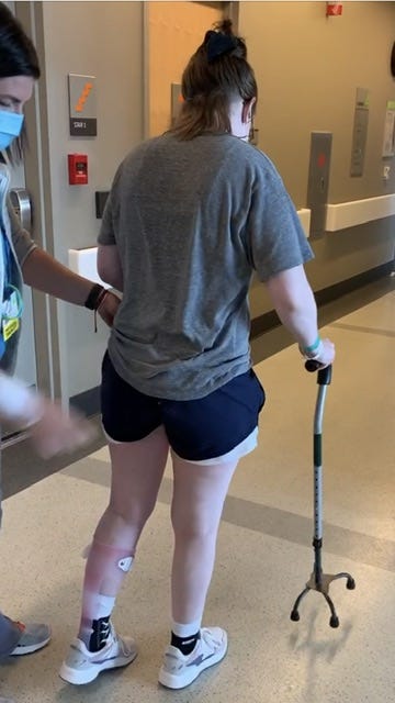 Author, pictured standing from behind. Holding a cane and being held by a PT