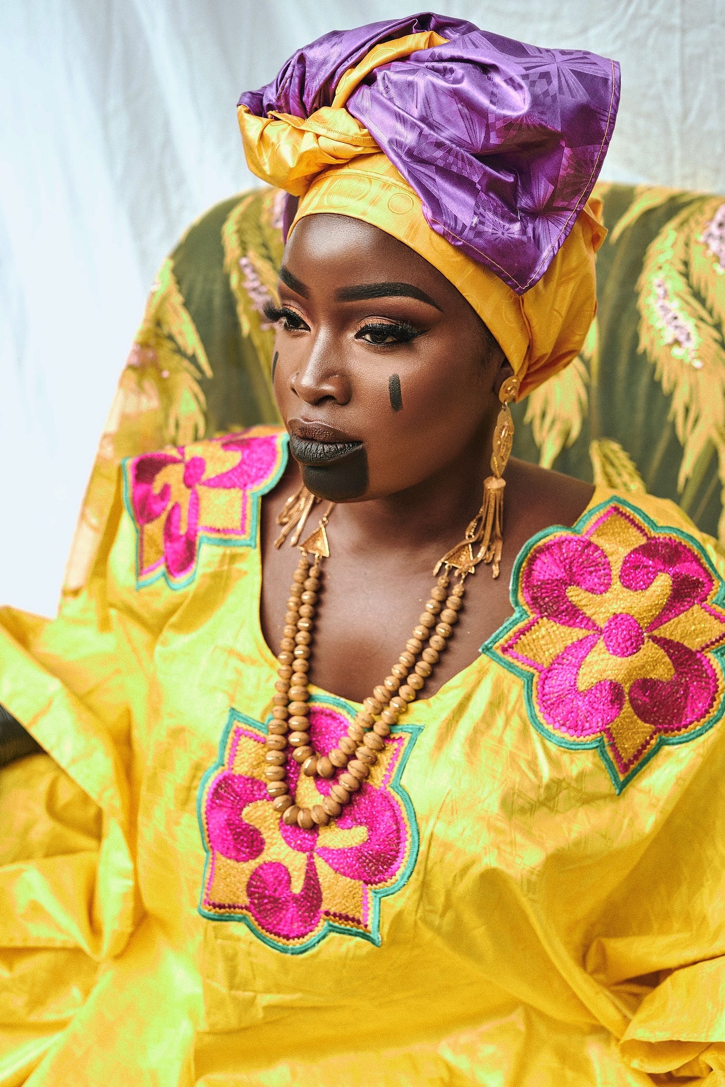 Lovette Jallow in a gold embroidered boubou, honoring West African scarification and oral governance. Lovette Jallow in a gold embroidered boubou, honoring West African scarification and oral governance.