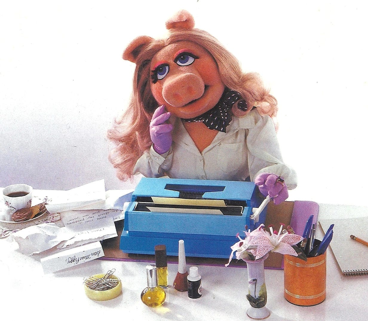 An image of Miss Piggy, looking very mindful, very demure, sitting in front of a vintage word processer.