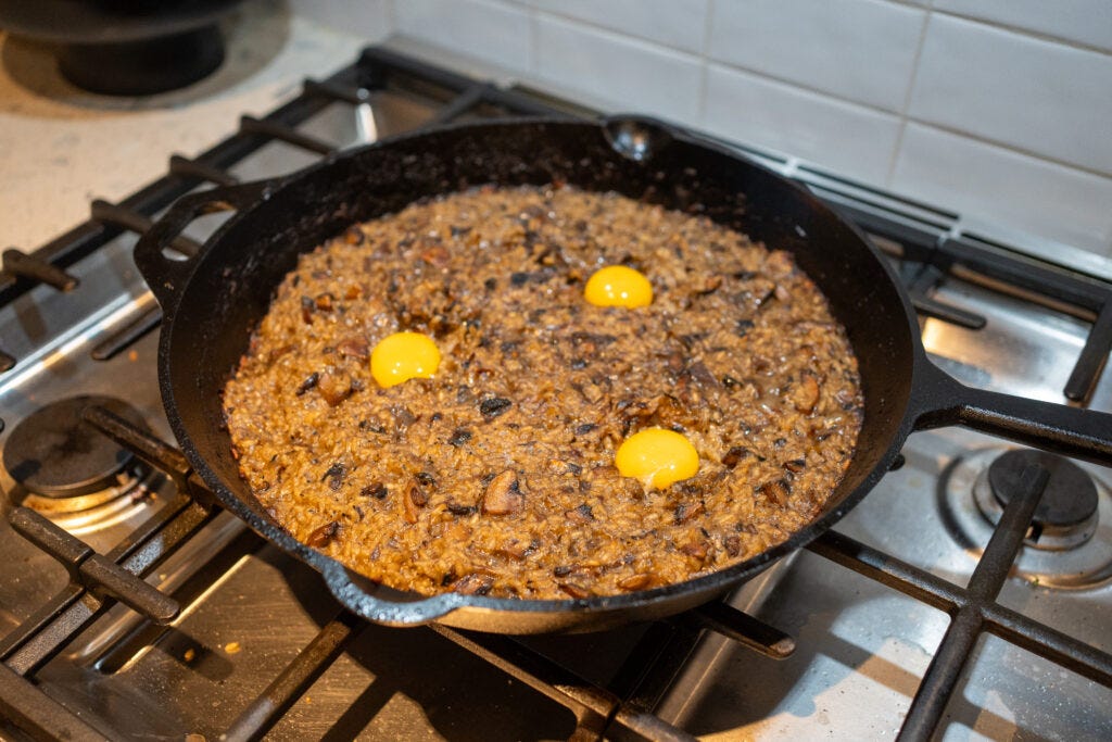 Three vibrant, raw egg yolks resting on top of a dark, scorched, and crispy broiled cast iron mushroom rice.