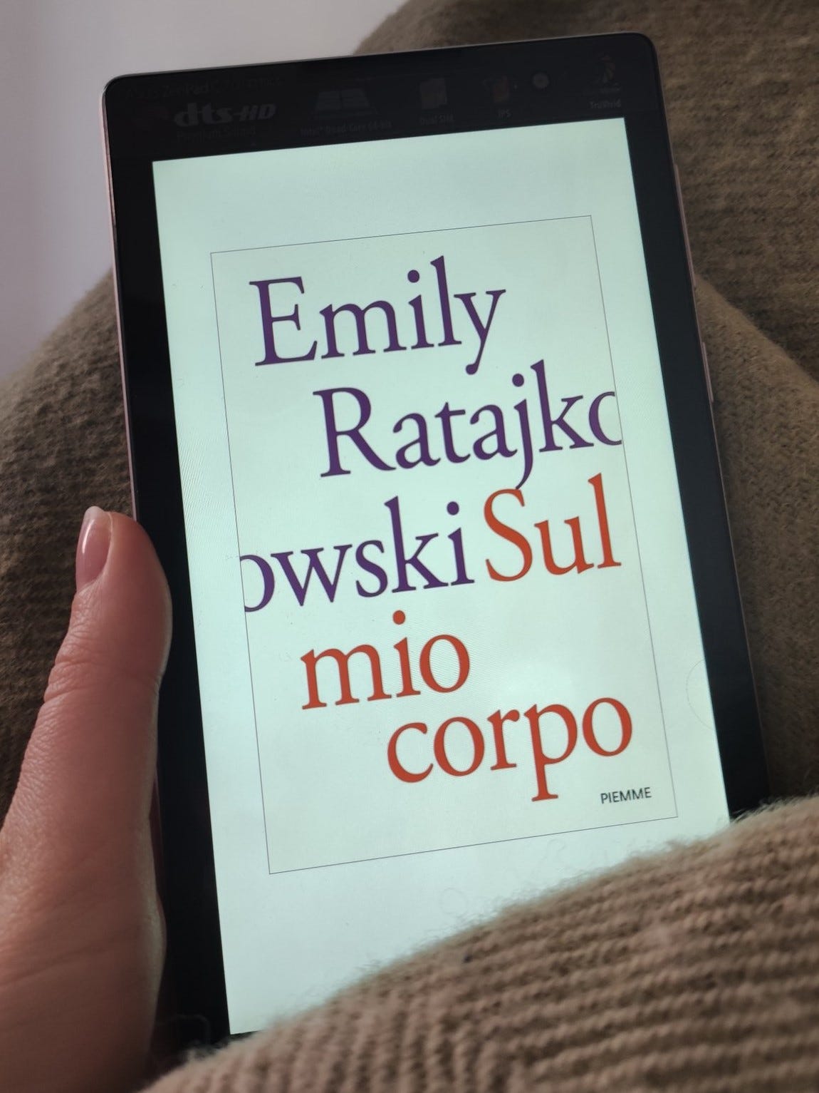 Una mano tiene un ebook, circondata da una coperta di lana verdina