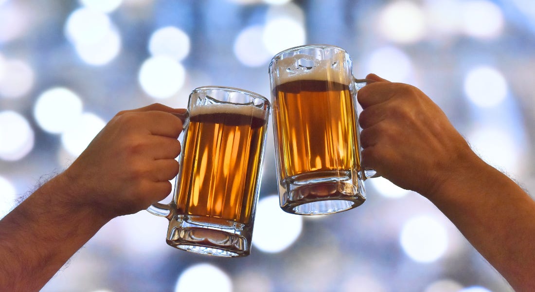 Two beer steins clinking together being held by two hands, with a glittery background