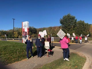 a group of picketers stand on the sidewalk holding signs 