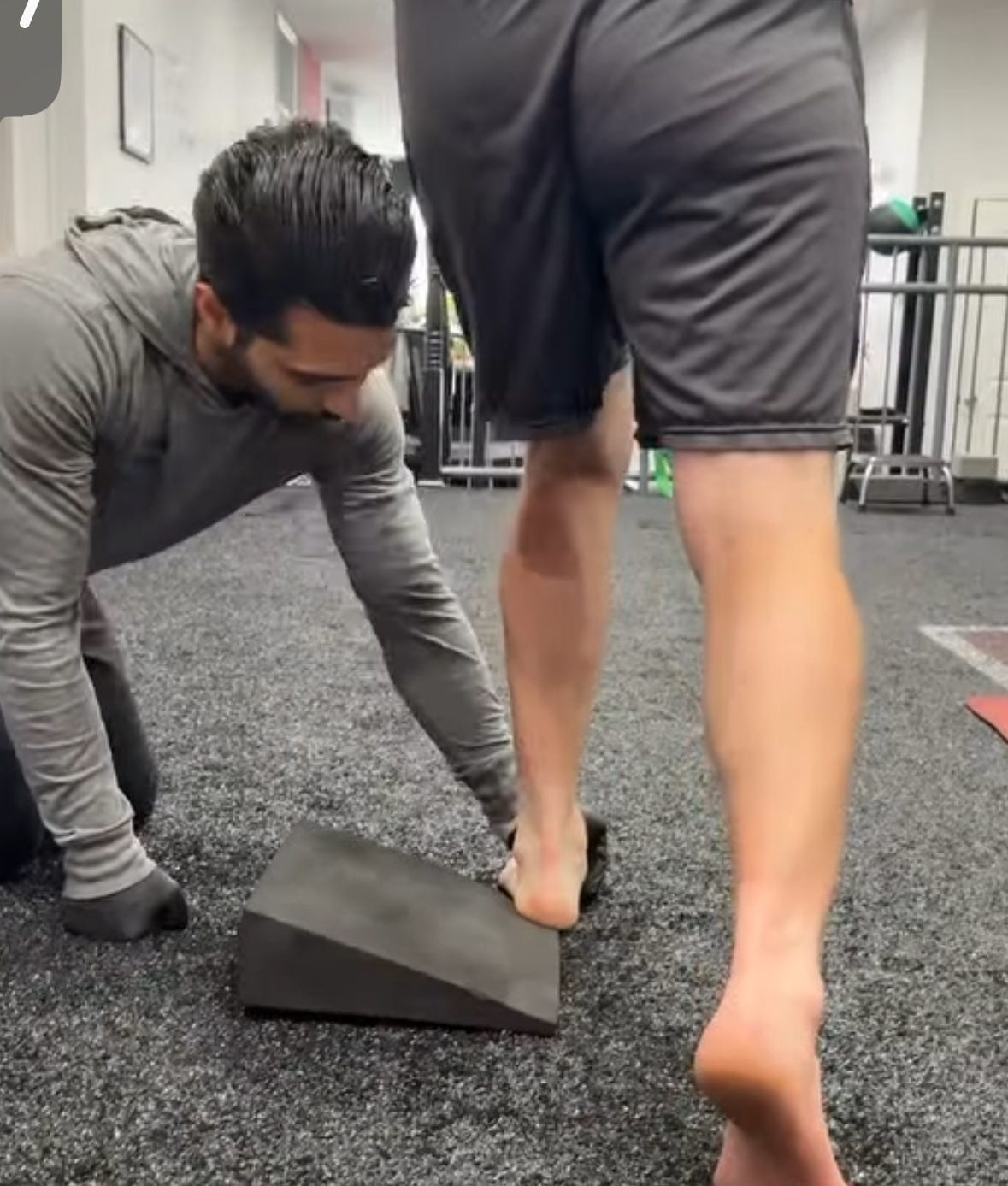 A physio works on foot alignment with a client in standing, using a slanted wedge. A physio works on foot alignment with a client in standing, using a slanted wedge.