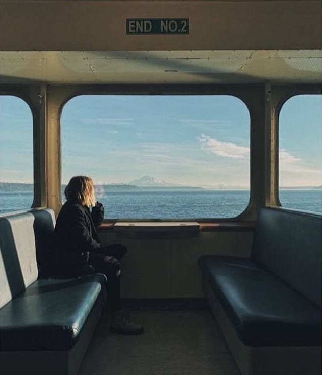 This may contain: a person sitting on a train looking out the window at the ocean and mountains in the distance