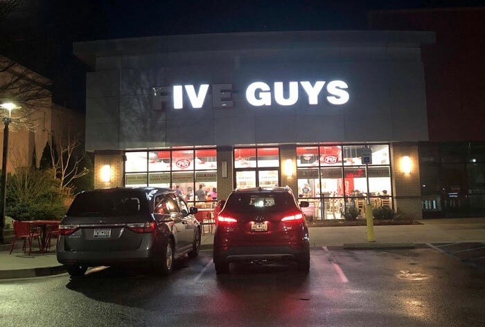 Obrázek pobočky FIVE GUYS, kde svítí pouze písmena IV GUYS