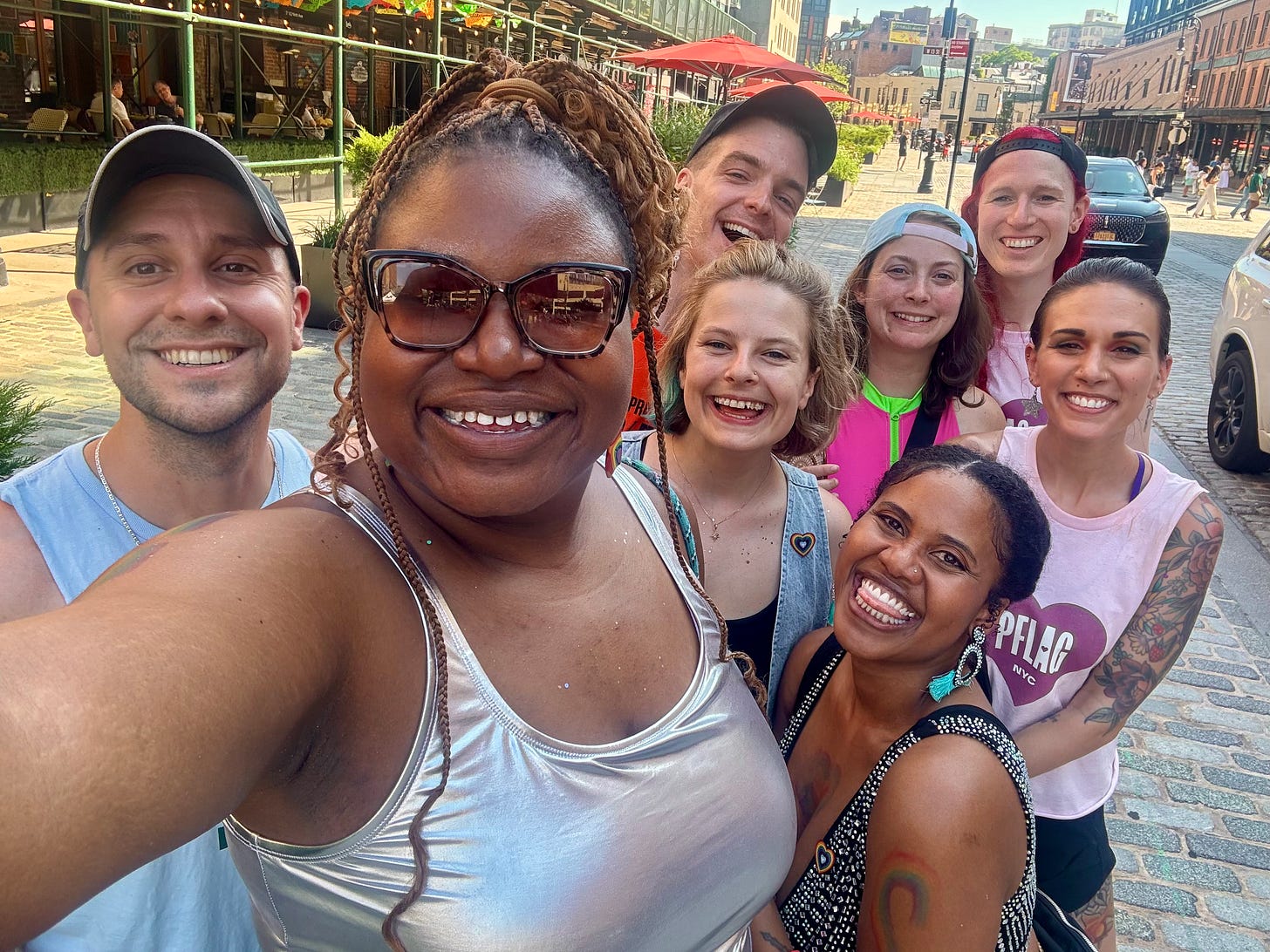 Shohreh surrounded by a diverse group of smiling queer friends taking a photo together outside a restaurant