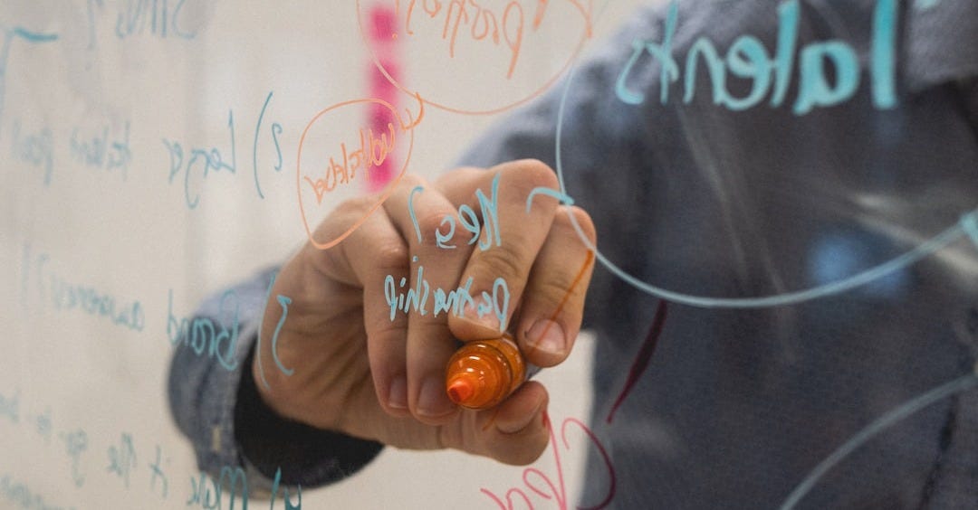 person writing on glass whiteboard with diagrams