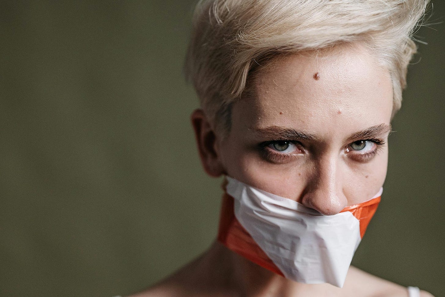 person with short platinum blond hair wearing a tight face mask or tape. Their nose is not under the mask, but their mouth is covered. The person looks unhappy. person with short platinum blond hair wearing a tight face mask or tape. Their nose is not under the mask, but their mouth is covered. The person looks unhappy.