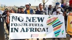 About 25 people stand with a banner that says 'No new fossil fuels in Africa!' and a large map of Africa About 25 people stand with a banner that says 'No new fossil fuels in Africa!' and a large map of Africa