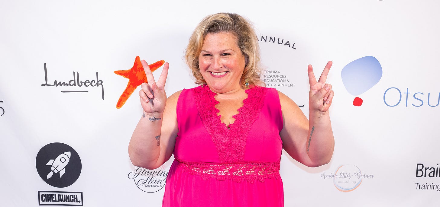 Jamie in a pink dress, smiling and making two peace signs Jamie in a pink dress, smiling and making two peace signs