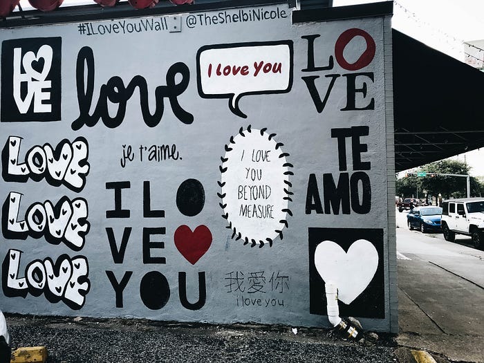 A brick wall covered in graffiti. The words ‘love’, or “I love you” are painted all over it in several languages.