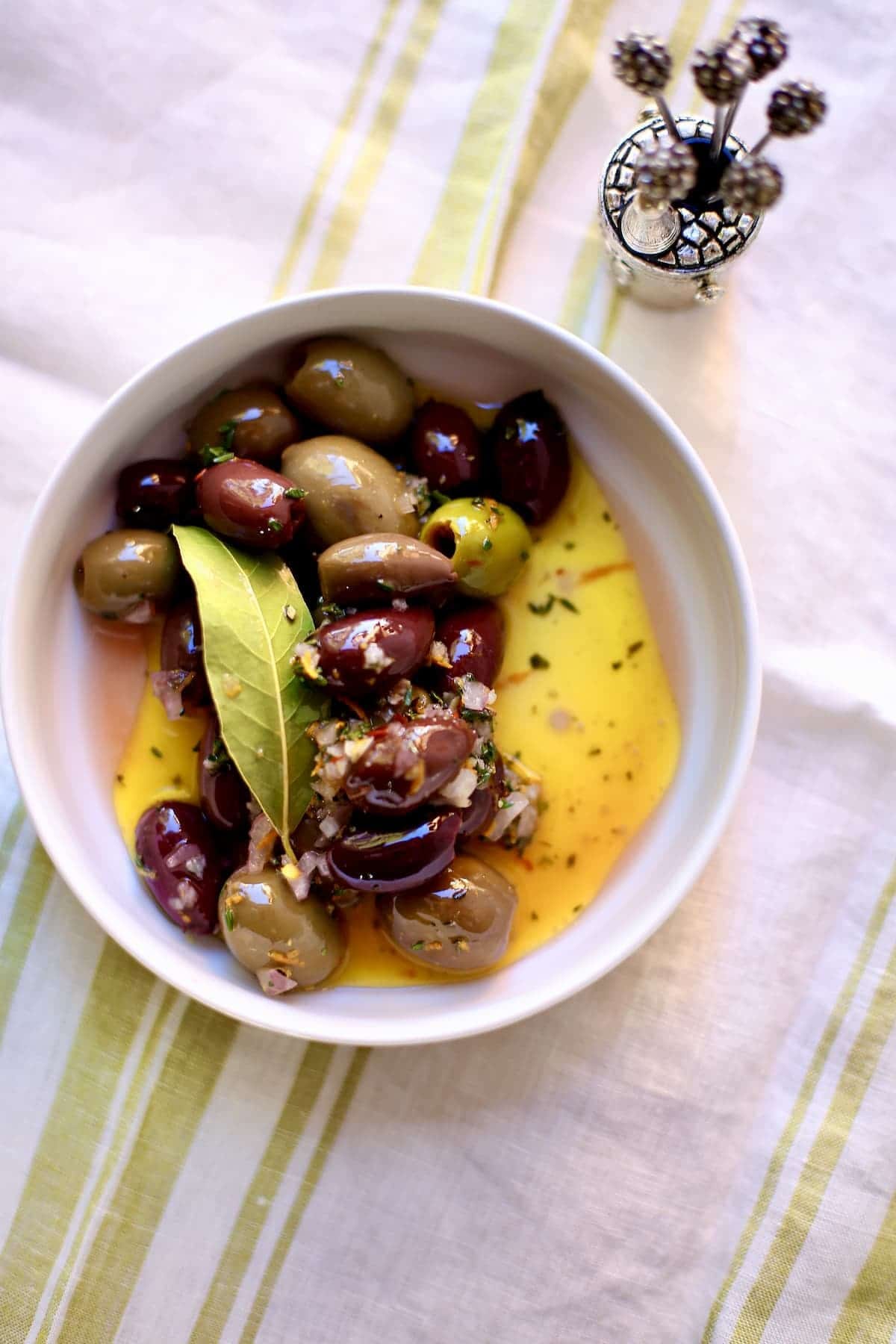 a bowl of olives with bay leaf and olive oil in a white bowl on a table a bowl of olives with bay leaf and olive oil in a white bowl on a table