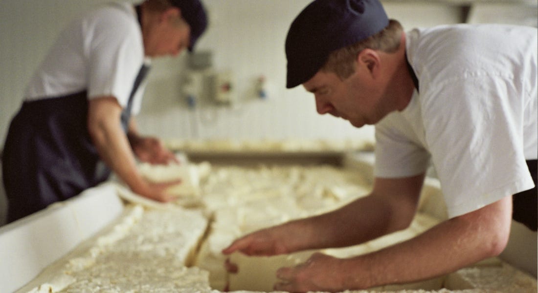 Two men working on a board filled with soft cheese Two men working on a board filled with soft cheese