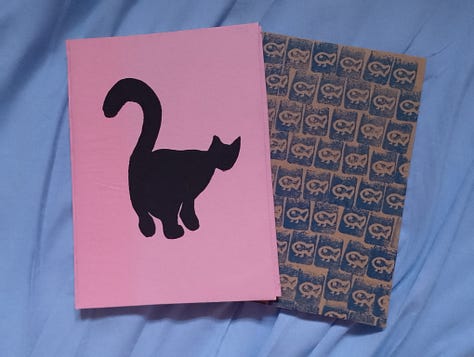 Grade de fotos mostra quatro cadernos, um preto, um azul com carimbos azul escuros em formato de caveira, um rosa com um gato preto pintado e um marrom com carimbos azuis de um peixe com pernas