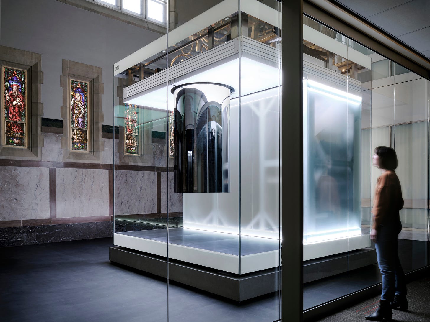 A person looks through a window at a quantum computer. A person looks through a window at a quantum computer.
