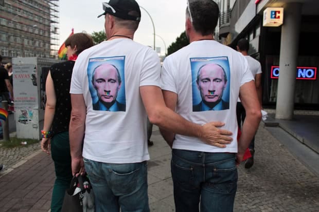 A gay couple wearing matching T-shirts printed with an image of Vladimir Putin, featuring a moustache in the colors of the LGBTQ+ flag, walk arm in arm during the STOP HOMOPHOBIA demonstration in Berlin on August 31, 2013. The protest, organized by the group ENOUGH IS ENOUGH, called for a boycott of the Sochi Olympics over Russia’s anti-gay propaganda laws.