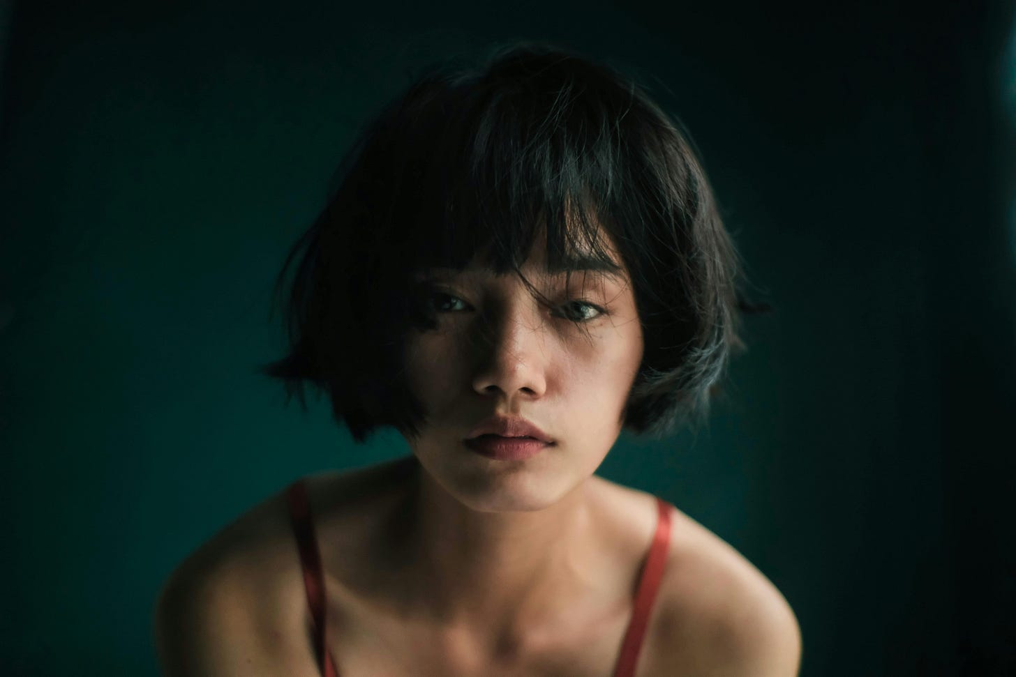 Free Sad young Asian female in red top looking at camera in studio with green wall Stock Photo