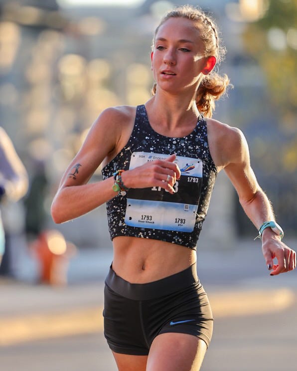 Fast woman running the Naperville half marathon. She wins the race. She wears Nike shorts and a Garmin running watch. 