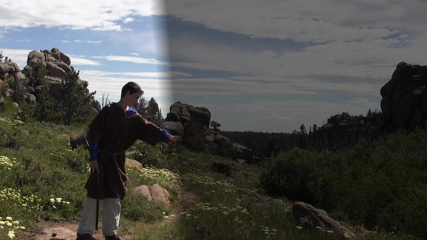 A young Caleb Quinn dressed in a tunic and holding a bow stands in front of the border of light and dark. The backdrop of foliage and boulders has been digitally altered so that half of the image is bright and the other half is dark. Caleb's character reaches his hand across the border to touch the darkness. A young Caleb Quinn dressed in a tunic and holding a bow stands in front of the border of light and dark. The backdrop of foliage and boulders has been digitally altered so that half of the image is bright and the other half is dark. Caleb's character reaches his hand across the border to touch the darkness.