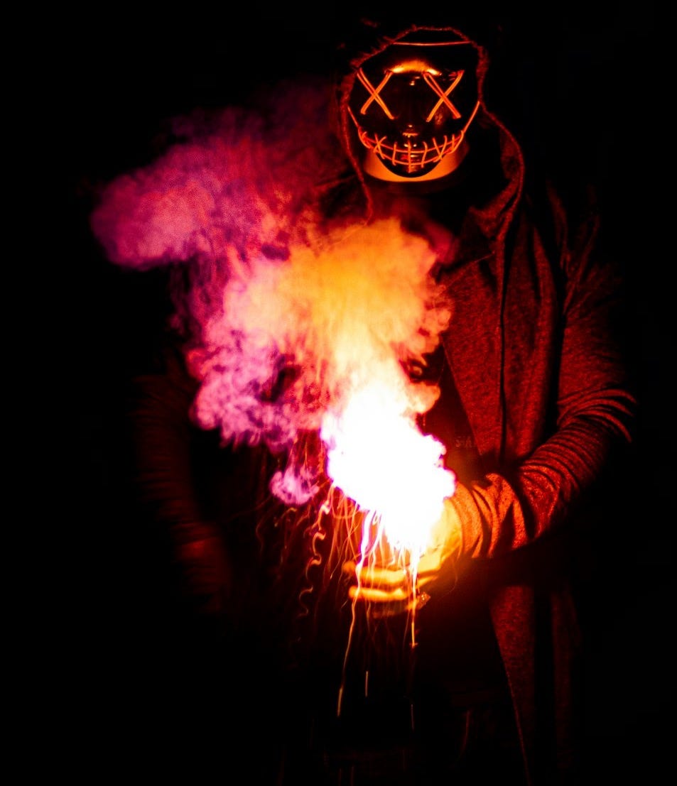 person in black mask holding purple and pink smoke