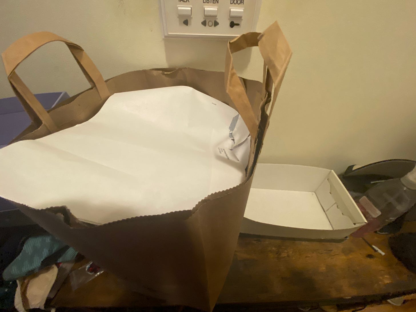 This image is of a paper grocery bag full of recylable mail in the foreground. In the background is an empty, warped, off-white shoebox.