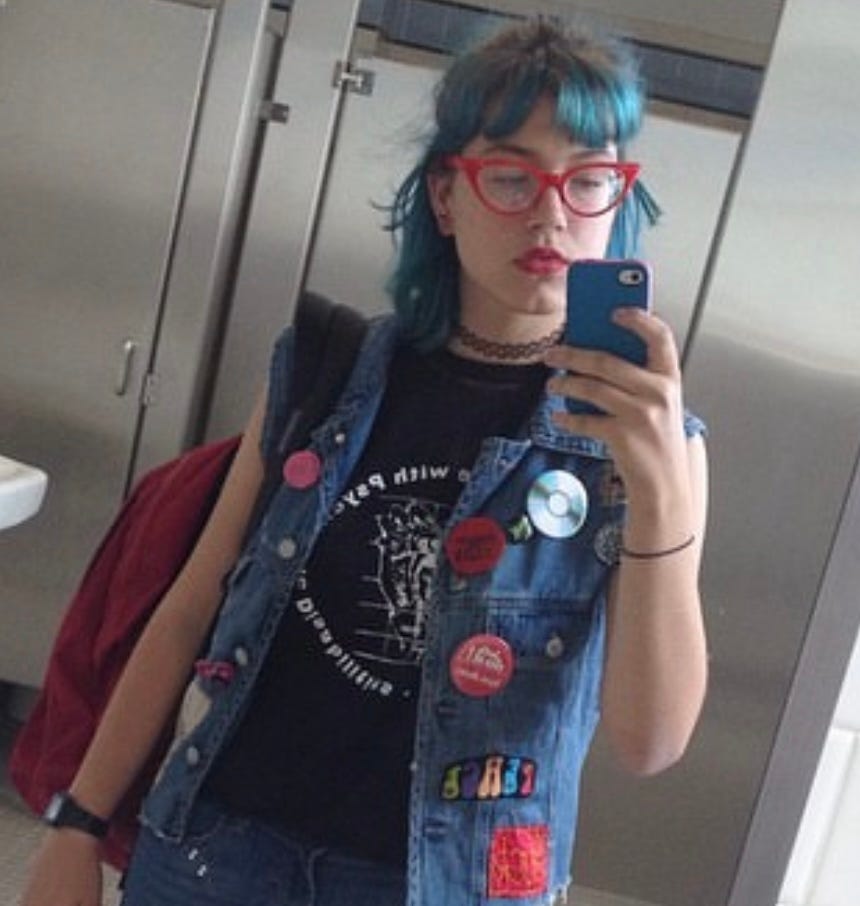selfie of the author with bright teal shoulder length hair & bangs and red cat eye glasses