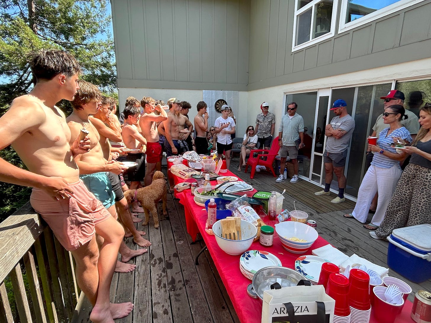 Aaron giving a heartfelt speech to the SRHS Varsity baseball team in a shaded backyard, players gathered around, drinks in hand, laughter in the air.