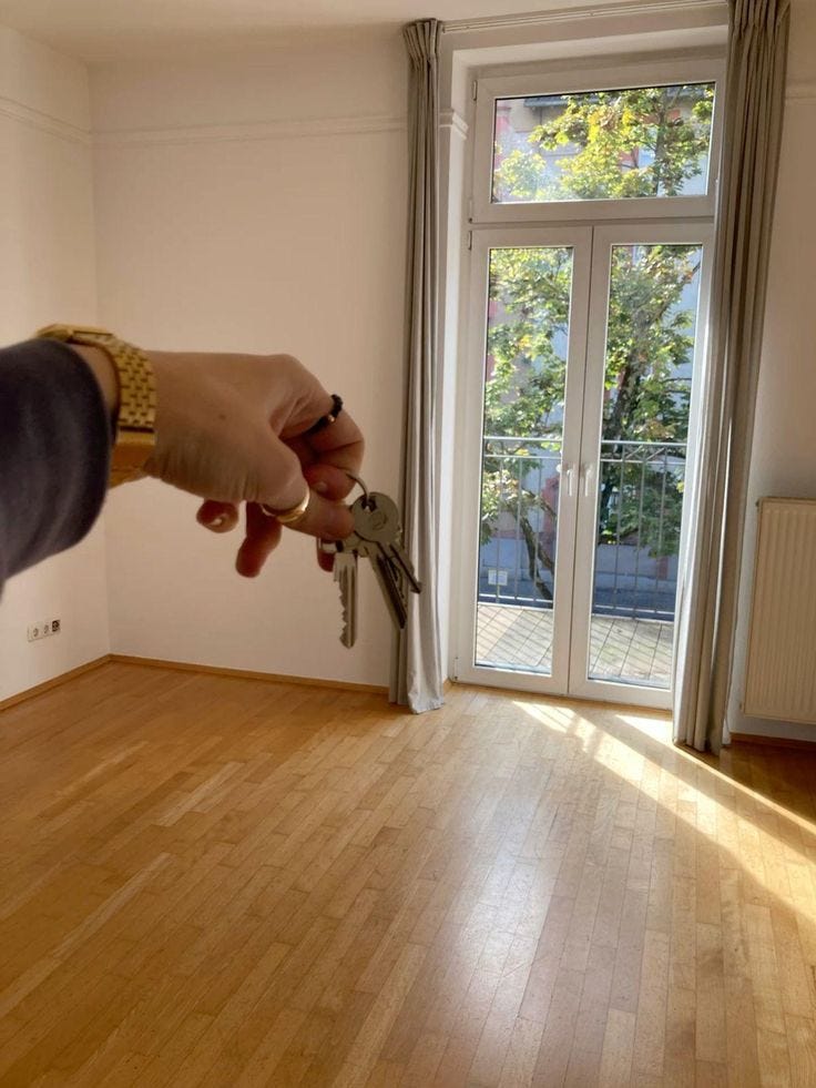 This may contain: a person holding a key in their hand while standing on a hard wood floor next to a window This may contain: a person holding a key in their hand while standing on a hard wood floor next to a window
