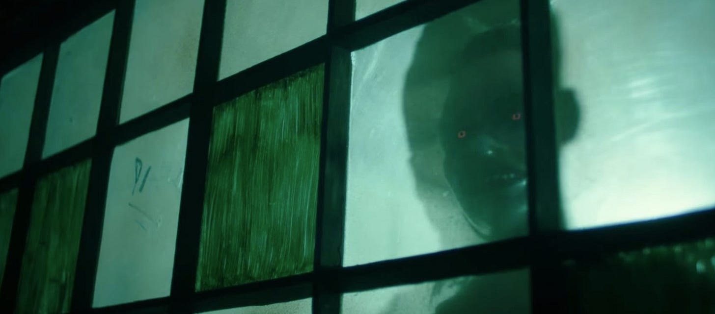 A grimy, frosted window. Through it, the sillhouette of a person with glowing red irises smiles.